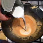 wlewanie mleczka kokosowego do woka z pastą curry i mleczkiem kokosowym