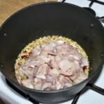 w garnku smaży się drobno siekana cebula i kawałki mięsa z kurczaka