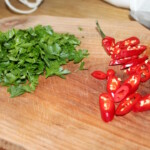posiekana natka pietruszki oraz pokrojone czerwone chilli na desce kuchennej