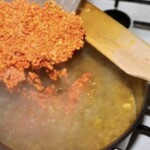 czerwona soczewica wrzucana jest do garnka z zupą