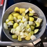 na patelni smażą się na oliwie kawałki ziemniaków, bakłażana i cebuli