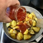 domowy przecier pomidorowy dodawany jest na patelnię ze smażącymi się kawałkami ziemniaków i bakłażana