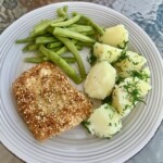 Dorsz w panierce z sezamem smażony podany z gotowanymi ziemniakami i zieloną fasolką szparagową na talerzu