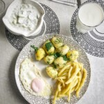 zielona fasolka szparagowa jajko sadzone oraz ziemniaki gotowane na talerzu. obok miska z mizerią oraz szklanka z kefirem